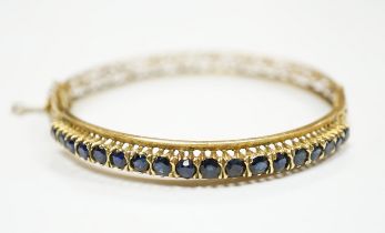 A pierced yellow metal and eighteen stone sapphire set hinged bangle, interior diameter 58mm,