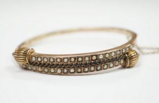 A Victorian yellow metal and two row seed pearl cluster set hinged bangle, gross weight 9 grams.