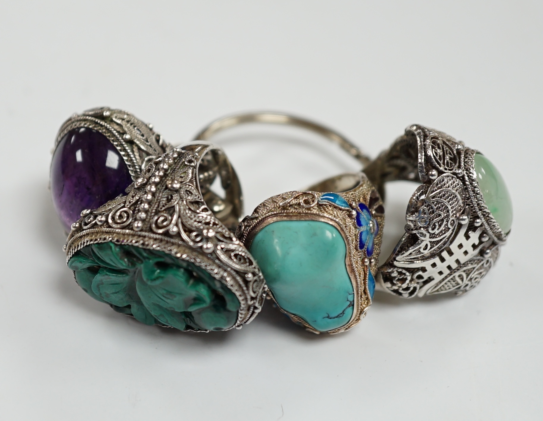 Four assorted Chinese white metal filigree and gem set rings, including turquoise and amethyst.