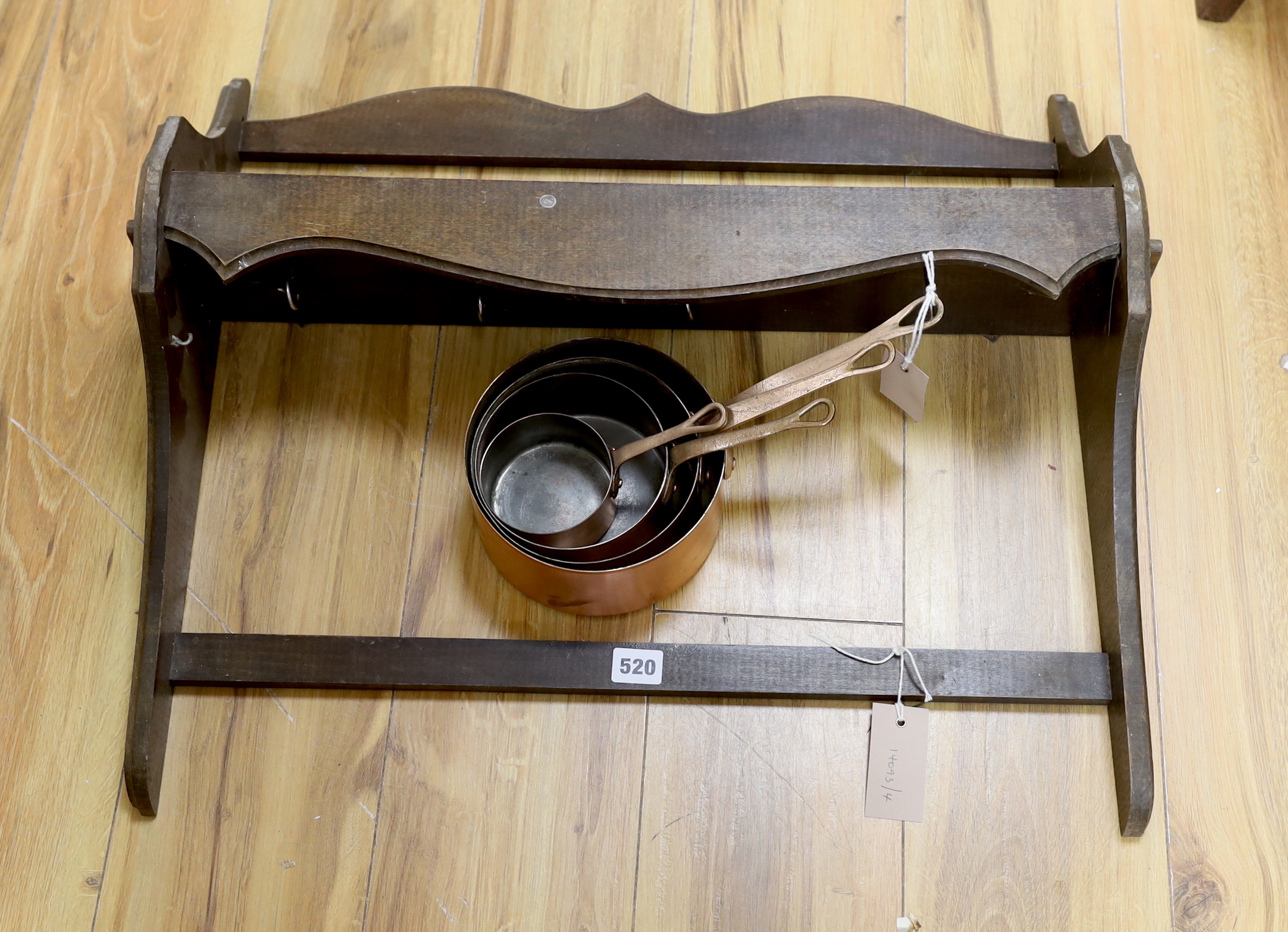 A graduated set of four copper and brass handled saucepans with a beech hanging wall rack, rack
