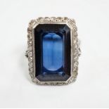 A 1920's white metal and single stone emerald cut synthetic sapphire set dress ring, with millegrain