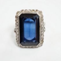 A 1920's white metal and single stone emerald cut synthetic sapphire set dress ring, with millegrain