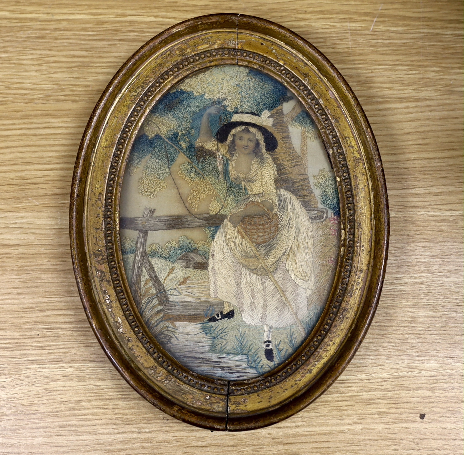 An early George IV oval silk work needlework pastoral embroidery, of a young girl with a fishing rod