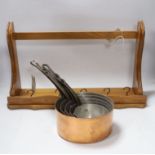 A graduated set of five French copper and cast iron saucepans with pine hanging rack, 57cm wide