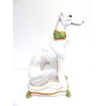 A LARGE GLAZED POTTERY MODEL OF A GREYHOUND SEATED ON A CUSHION white, with pale brown and green