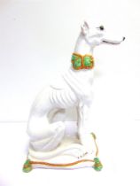 A LARGE GLAZED POTTERY MODEL OF A GREYHOUND SEATED ON A CUSHION white, with pale brown and green