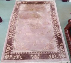 A pink ground Oriental style rug with stylized central medallion and spandrels within dark border,