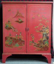 An early 20th century Oriental style two door cabinet painted red with village scenes to doors,