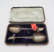 A cased pair of Dutch silver serving spoons, with cast figural stems, engraved with scrolling