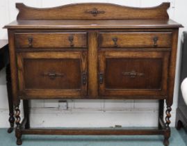 An early 20th century oak buffet with two drawers over pair of cabinet doors on barley twist