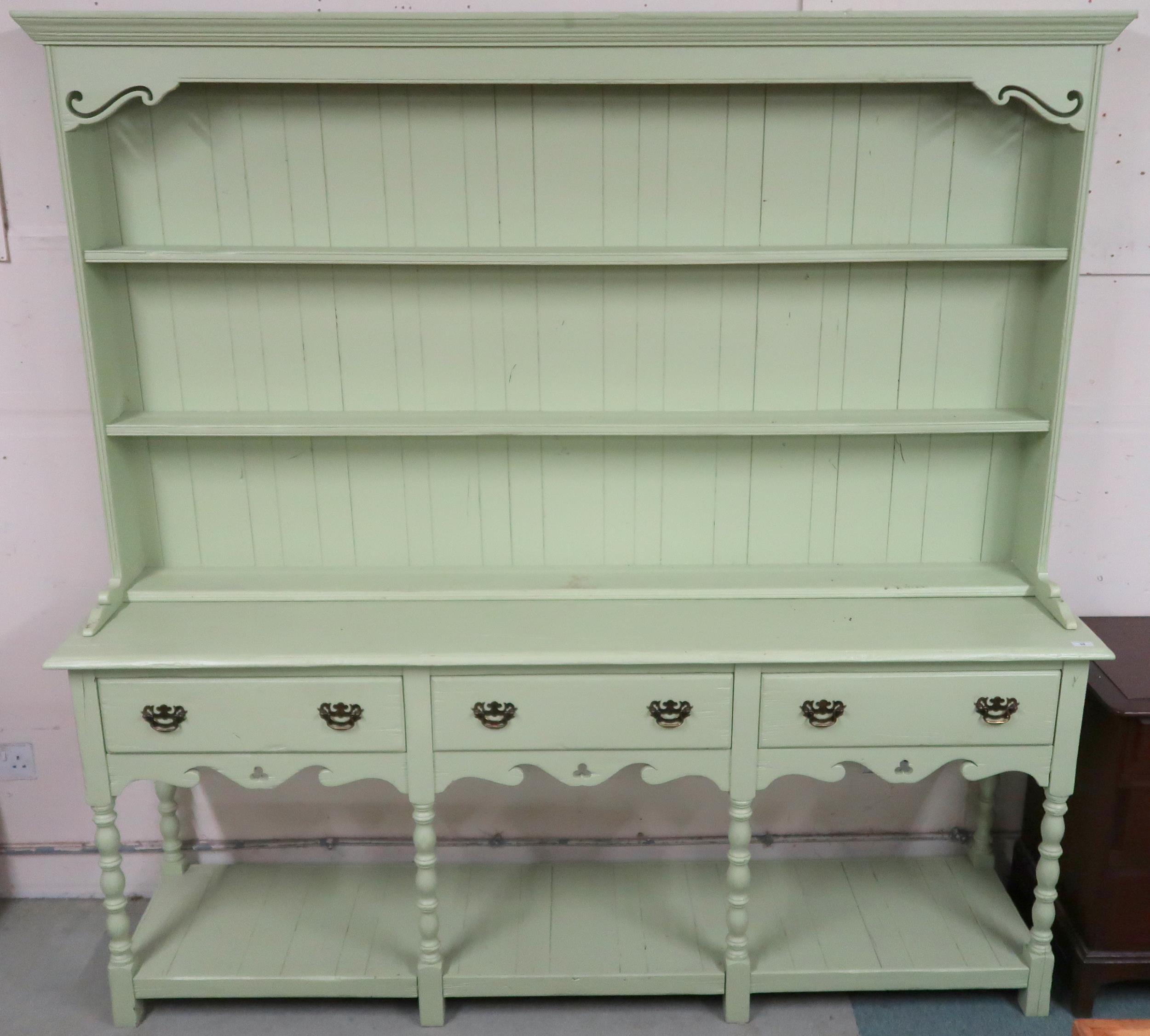 A pastel green painted Welsh style kitchen dresser with moulded cornice over two open shelves on