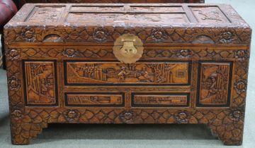 A 20th century Oriental camphor wood blanket chest carved with village scenes framed within floral