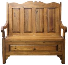 A 20th century stained pine hall settle with shaped surmount over panelled backrest flanked by