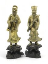 A PAIR OF CHINESE BRASS OFFICIALS Each standing and holding an object on a high rocky mound base,