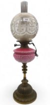 A brass and glass oil lamp with buttons marked for Young's screw fittings, with a pink milk glass