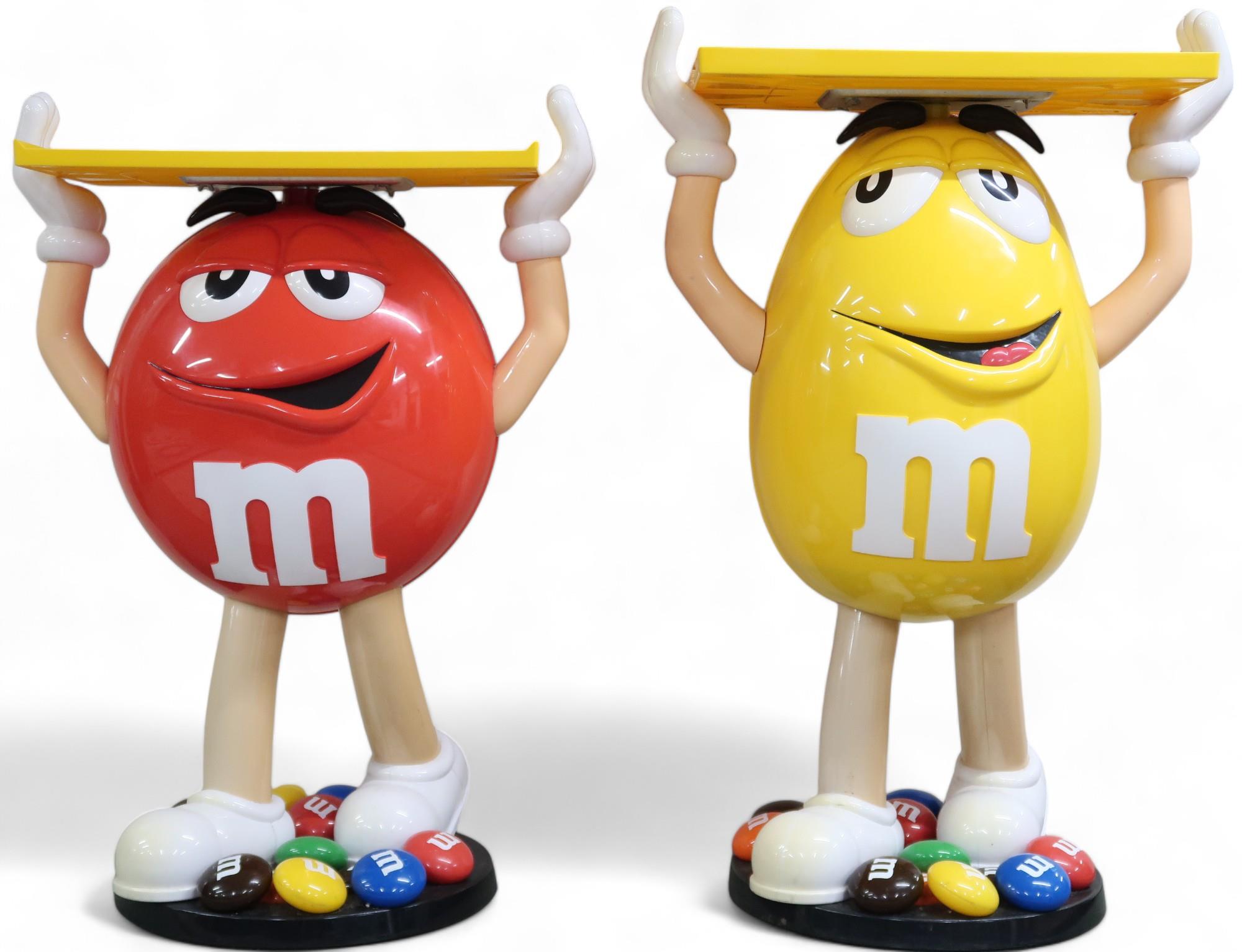 A lot comprising mixed pair of Mars M&M red and yellow advertising standees holding fixed serving