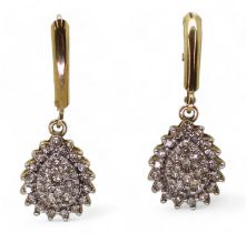A pair of 10k gold diamond drop earrings with continental hoop closure, set with estimated approx