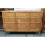 A mid 20th century elm and beech Ercol style sideboard with shaped top over three short drawers over