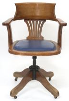 An early 20th century oak swivel desk chair with hoop back over blue upholstered seat on revolving