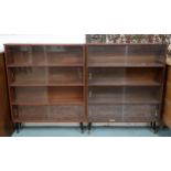 A pair of mid 20th century stained teak bookcases with glass sliding doors on ebonised supports,