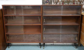A pair of mid 20th century stained teak bookcases with glass sliding doors on ebonised supports,