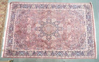 A pink ground Tabriz rug with dark blue sunburst central medallion and matching spandrels on a