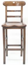 A 20th century stained beech tall clerks stool with laddered back over shaped seat on square