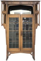 AN OAK ARTS & CRAFTS LEADED GLASS BOOKCASE IN THE MANNER OF E A TAYLOR with top frieze carved with