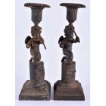 A RARE PAIR OF EARLY 19TH CENTURY FRENCH CAST IRON CANDLESTICKS formed as putti holding bows, upon