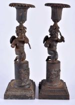 A RARE PAIR OF EARLY 19TH CENTURY FRENCH CAST IRON CANDLESTICKS formed as putti holding bows, upon