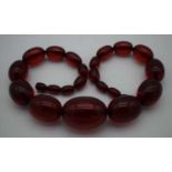 A LARGE CHERRY AMBER TYPE NECKLACE. 77 grams. 45cm long, largest bead 3.5 cm x 2.5 cm.