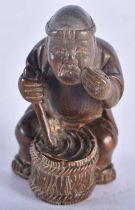 A Japanese Carved Hardwood Netsuke in the form of a Seated Male stirring a cooking pot. 5.5 cm x 3.5