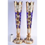 A VERY LARGE PAIR OF CONTINENTAL FLORAL EMBELLISHED BLUE AND GILT GLASS VASES. 58 cm high.