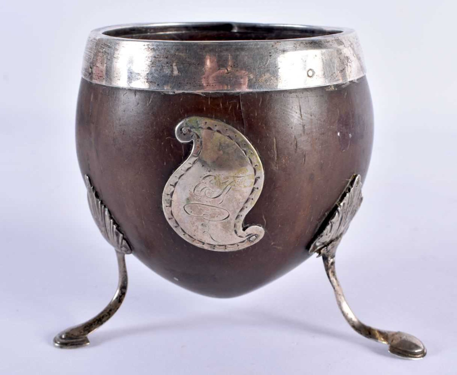 A GEORGE III WHITE METAL MOUNTED COCONUT CUP formed with a scrolling cartouche, upon splayed legs.