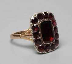 AN EARLY VICTORIAN GARNET CLUSTER RING, the central trap cut stone within a border of fourteen mix