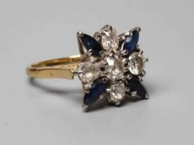 A SAPPHIRE AND DIAMOND DRESS RING, the central cushion cut diamond claw set within a border of