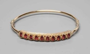 A STIFF HINGED BANGLE, the upper section claw set with ten oval facet cut garnets, indistinctly