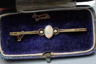 AN EDWARDIAN OPAL AND SEED PEARL BAR BROOCH, the claw set oval cabochon polished opal flanked by two