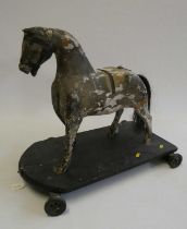 An antique carved wood pull-a-long horse, with horse hair tail, wooden base and metal wheels, 23 3/