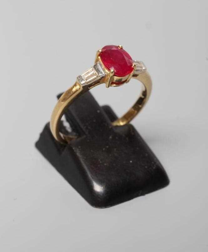 A RUBY AND DIAMOND RING, the oval facet cut ruby claw set to tapering shoulders, each channel set