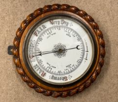 An oak cased aneroid barometer circa 1920's with a ceramic dial, a rope twist design carved case and