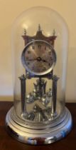 A chrome anniversary clock under a glass dome, complete with key. 30cm h.