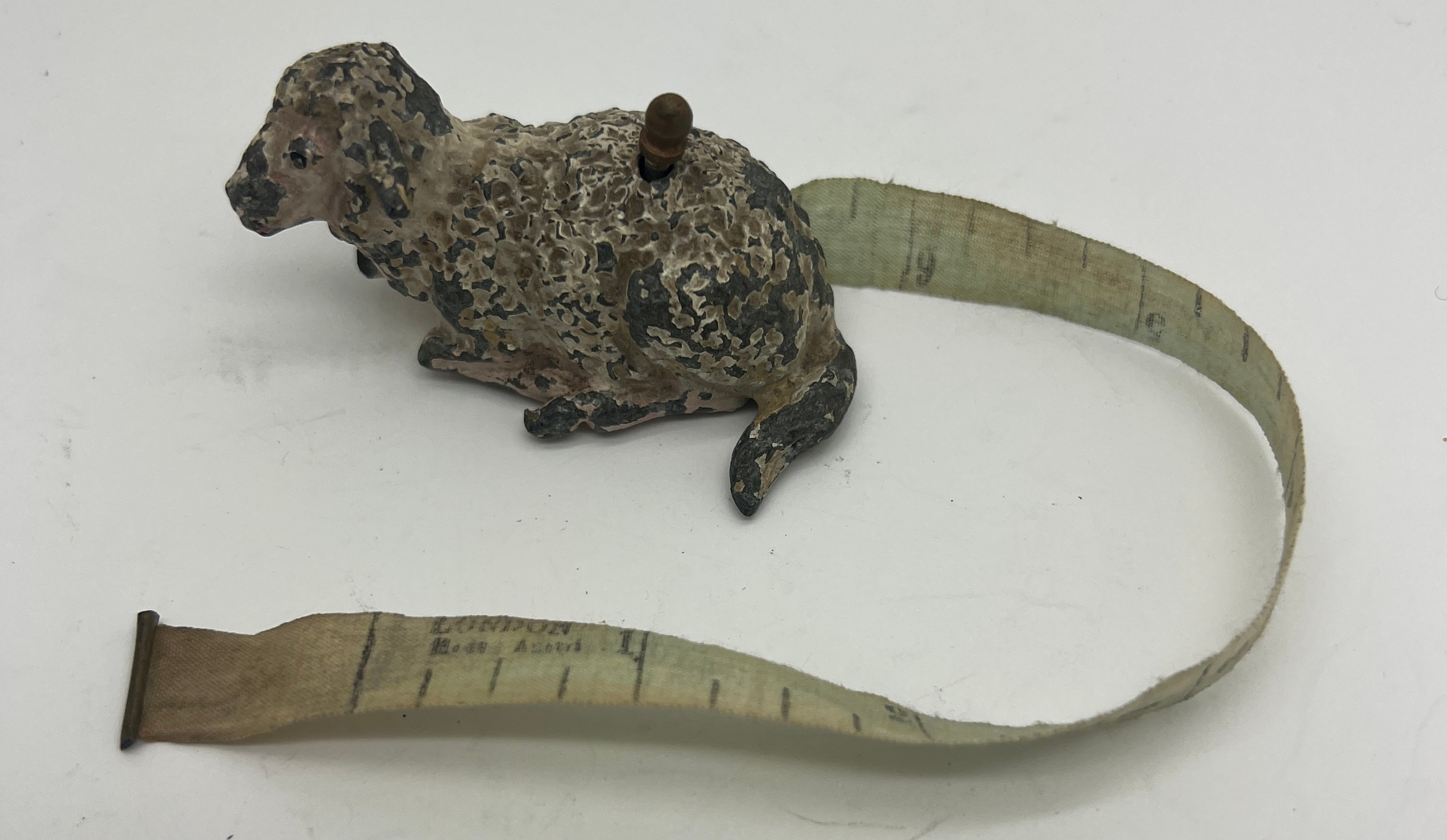 An early 20thC metal sheep tape measure. 5cm l. Measures centimetres and inches.
