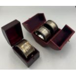 Three napkin rings, two silver plated and one silver in fitted leather cases.