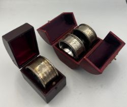 Three napkin rings, two silver plated and one silver in fitted leather cases.