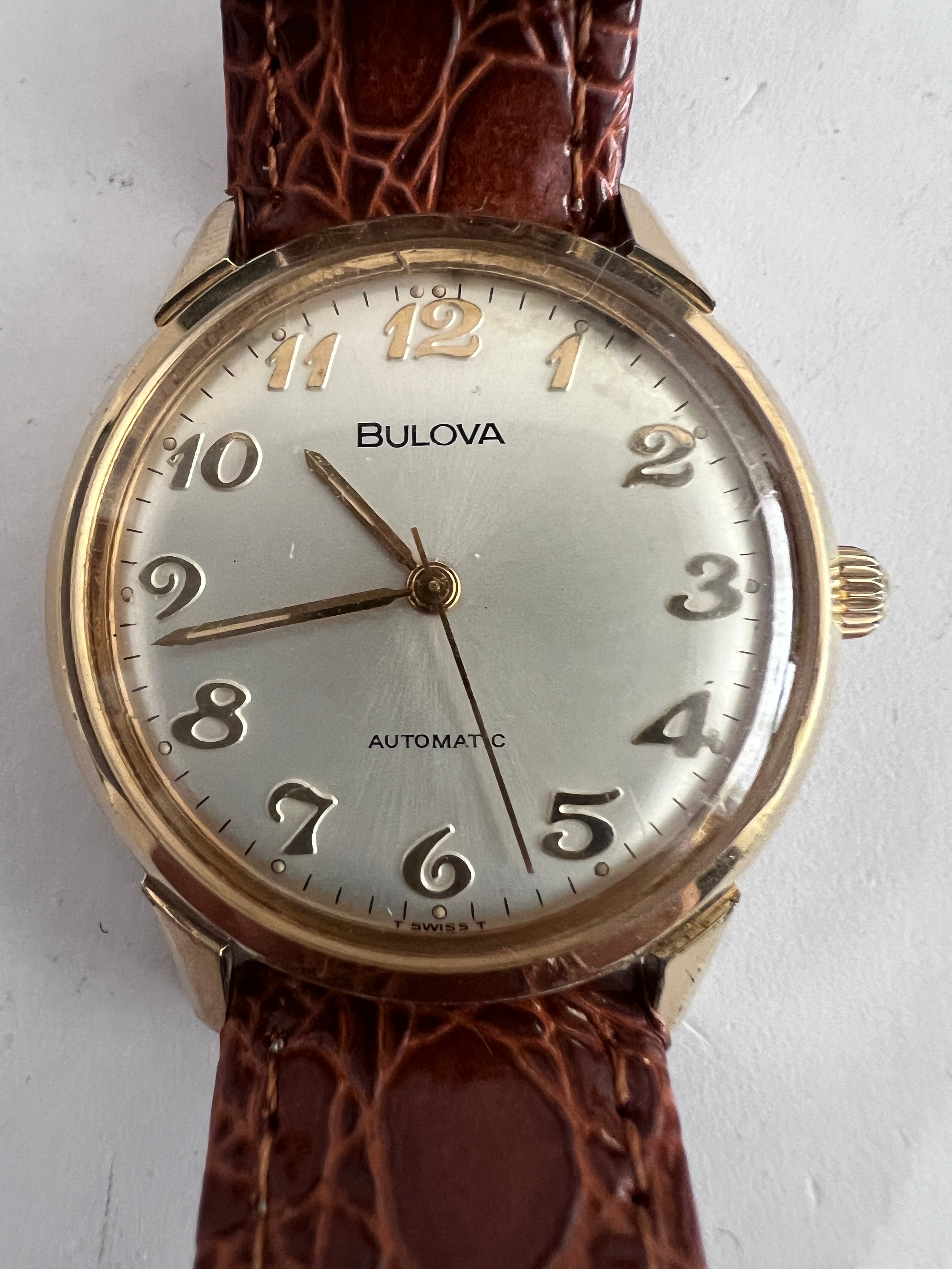A 1974 vintage automatic Bulova wristwatch, gold plated on brown leather strap with silver face.