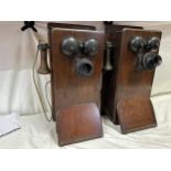 Two wooden cased wall mounted telephones, with mouth piece to the left hand side, crank handle to