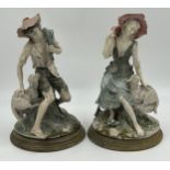 Two Giuseppe Armani Capodimonte figures of a lady and a gent, seated with sheep on wooden plinths.