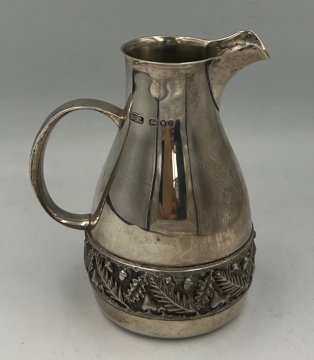 A hallmarked silver jug with acorn and leaf decorative band to base. London 1978, maker House of