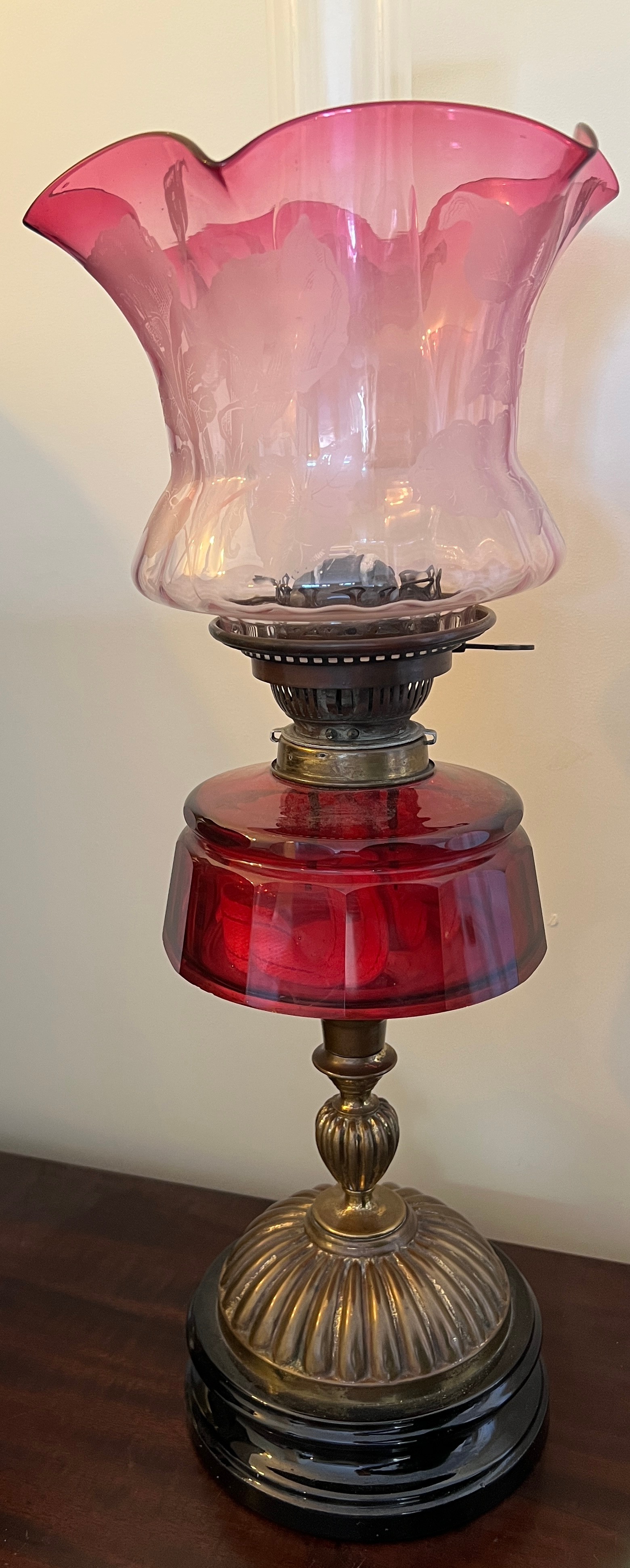 A 19thC brass and cranberry glass oil lamp with etched glass shade. 52cm h to top of shade.
